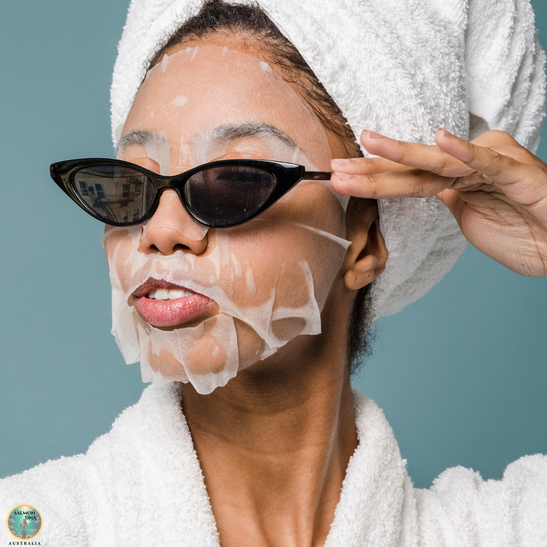 Woman wearing facial sheet mask and sunglasses with towel on head for post-treatment skincare care