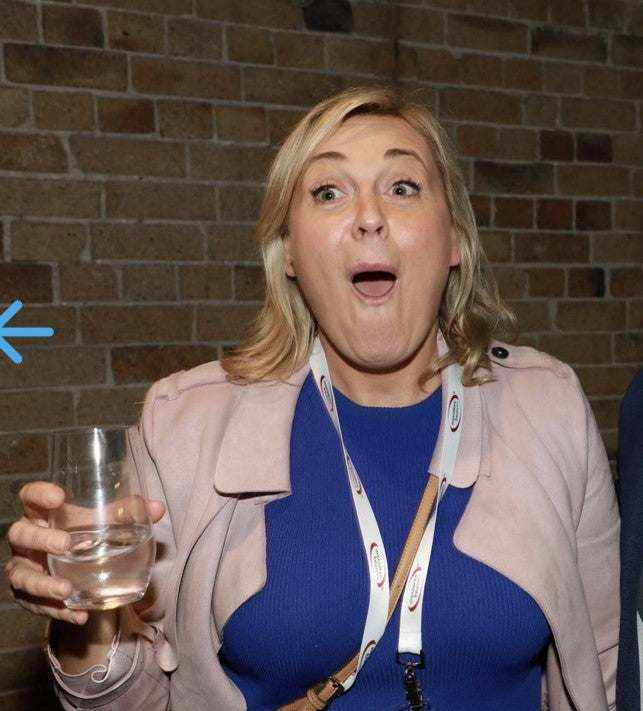 Woman with surprised expression holding a glass, representing confidence in cancer and skincare journey