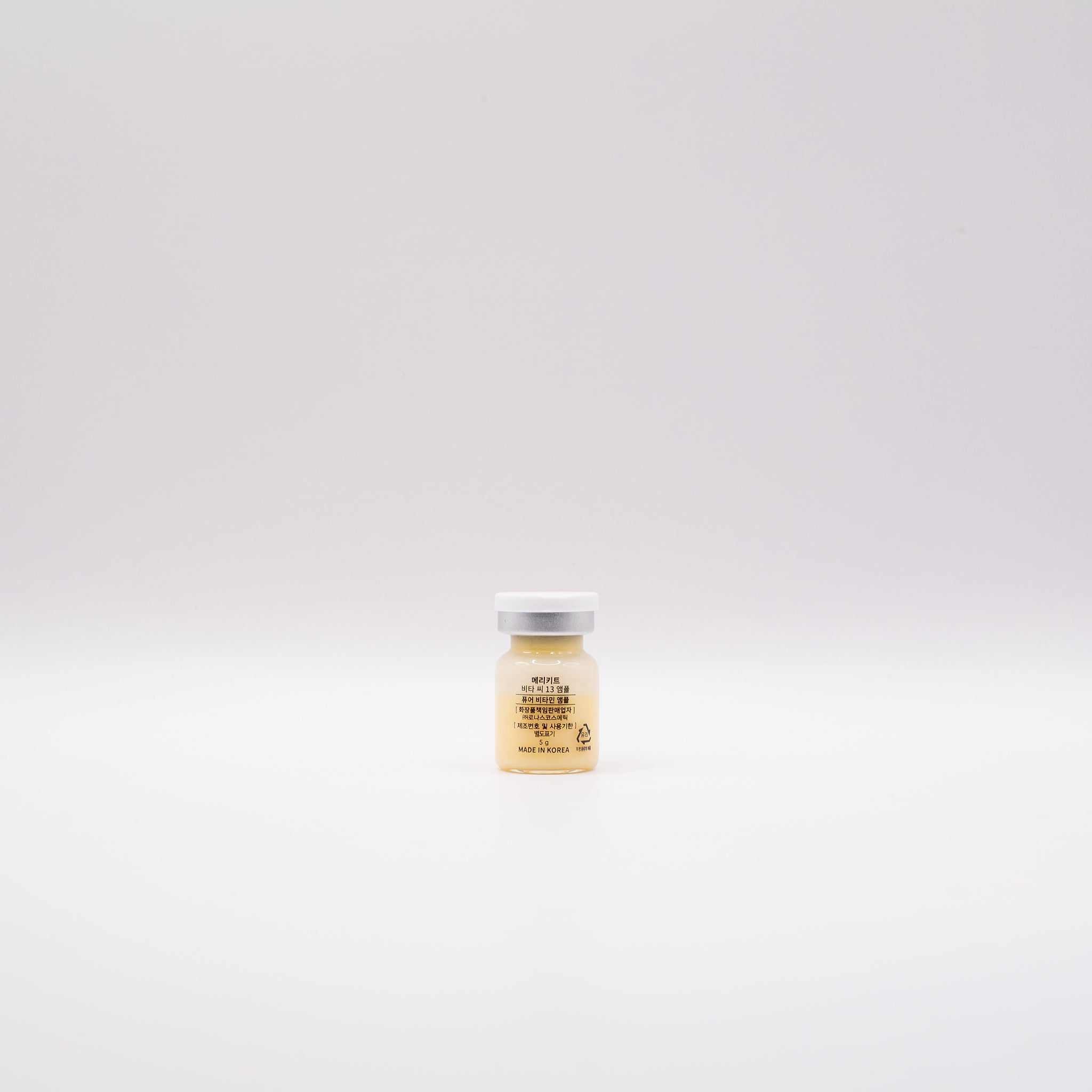 Single small clear glass ampoule bottle with white cap containing MERIKIT Vita-C 13 vitamin C serum against a plain white background