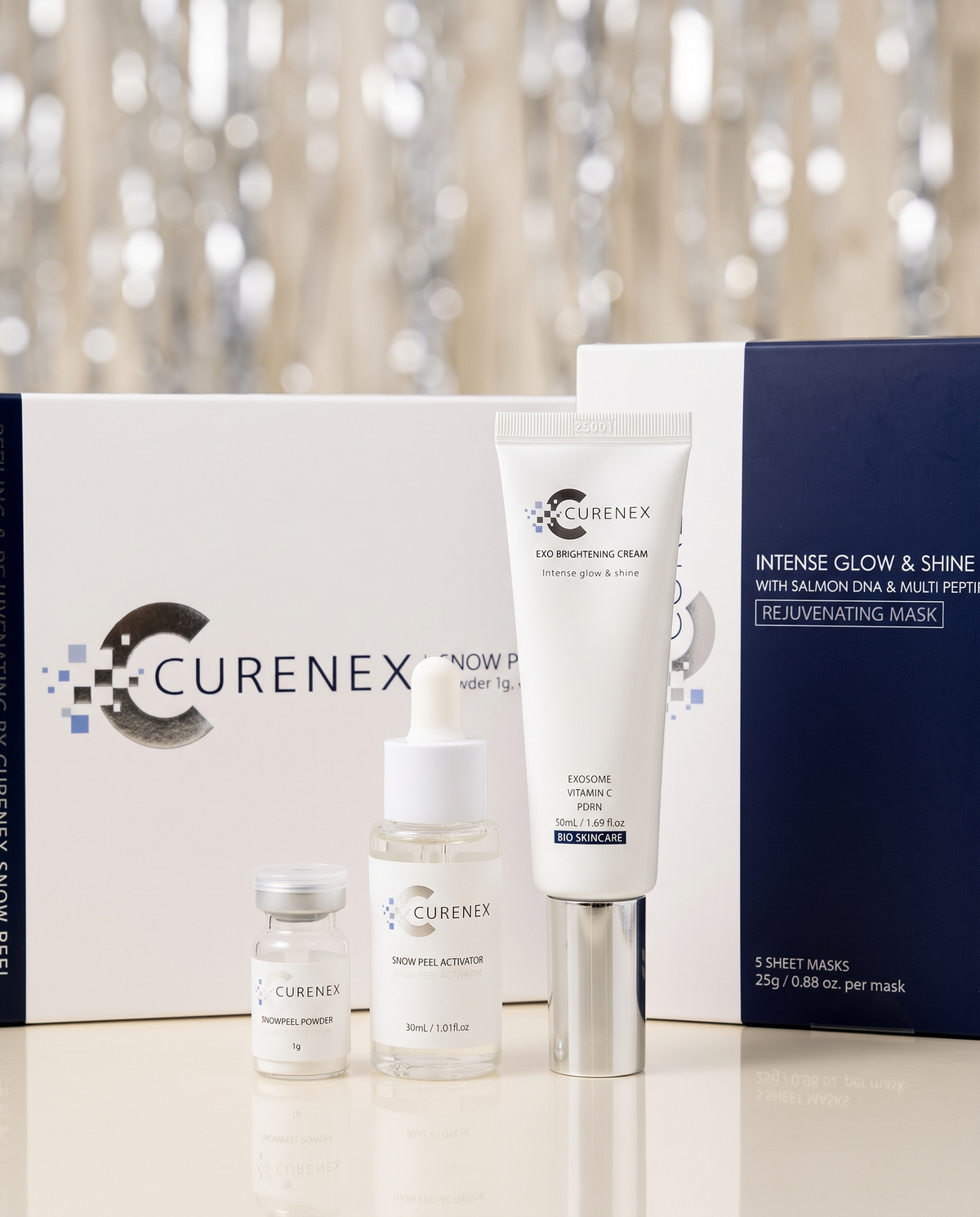 The Glow Night In Gift Set with white skincare tubes, glass dropper bottles and navy sheet mask box, packaged together.